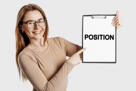 POSITION. Beautiful young business woman wearing glasses holds a clipboard with mock up space isolated on gray backgroundの写真素材