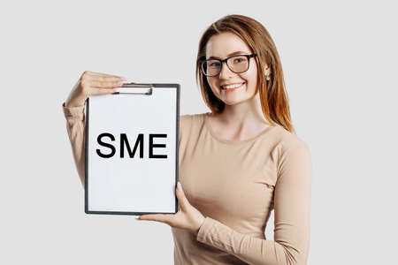 sme. Beautiful young business woman wearing glasses holds a clipboard with mock up space isolated on gray backgroundの写真素材