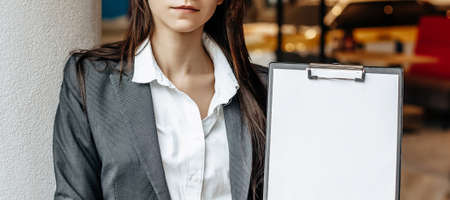 The woman shows information on the tablet. Place for advertising. Business concept. The girl holds the documents and explains the information. White blank sheet of paper.の写真素材