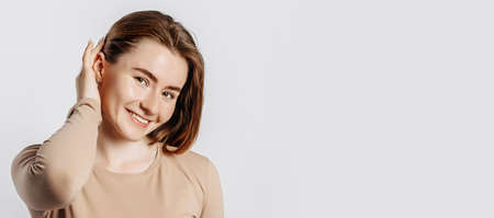 Beautiful young girl smiling and posing looking at the camera on a white isolated background. Positive brunette woman in a beige jumper. Kind look.の写真素材