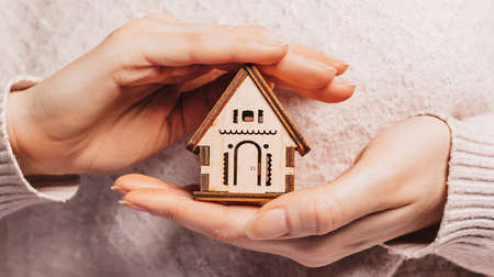 Woman holding a wooden house with her hands with the sun on a light pink background. Sweet homeの写真素材