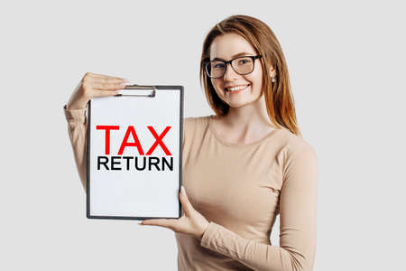 Tax return. Beautiful young business woman wearing glasses holds a clipboard with mock up space isolated on gray backgroundの写真素材