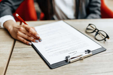 Young girl office worker or business lady signs documents. Concentrated businesswoman working with papers. Business conceptの写真素材