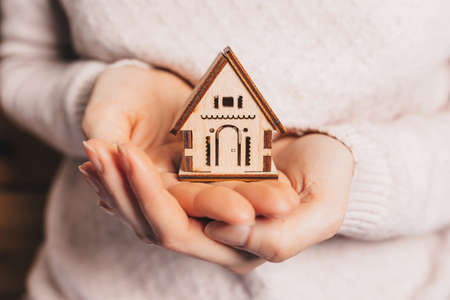 Woman holding a wooden house with her hands with the sun on a light pink background. Sweet homeの写真素材
