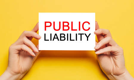 Female hands hold card paper with text PUBLIC LIABILITY on a yellow background. Business and finance conceptの写真素材