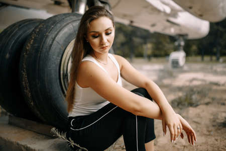 beautiful young brunette girl stands on the background of old military aircraft. Girl in a white...