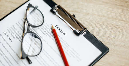 A contract on a wooden work table with glasses and a red pencil. The documents are ready for signing. Business concept. Collaboration agreement.の写真素材