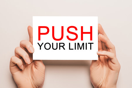 Female hands hold card paper with text PUSH YOUR LIMIT on a yellow background. Business and finance conceptの写真素材