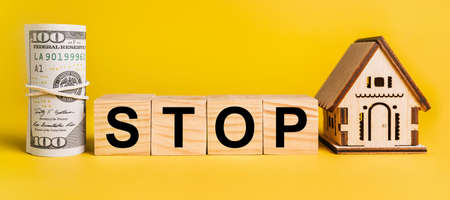 STOP with house miniature model and money on a yellow background. The concept of business, finance, credit, tax , real estate, home, housingの写真素材