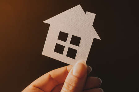 Woman holding a paper house with her hands backlit on a dark background. Sweet homeの写真素材