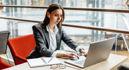 Girl works on a laptop in the workplace. Businesswoman is shocked by the crisis. Successful woman creates a startup and makes decisions.の写真素材