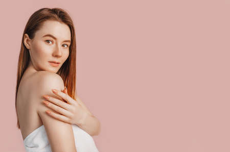 Beautiful sensual young girl with clean skin on a pink background with a mockup. Topless woman in a towel. The concept of spa treatments, natural beauty and care, youth, cream and mask, freshnessの写真素材