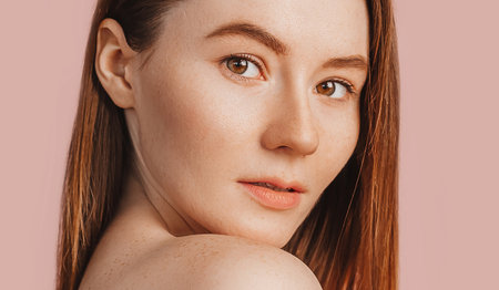 Beautiful sensual young girl with clean skin on a pink background with a mockup. Topless woman in a towel. The concept of spa treatments, natural beauty and care, youth, cream and mask, freshnessの写真素材