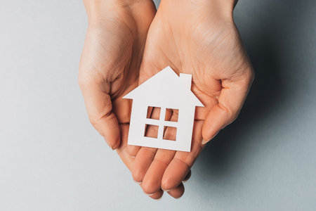 Woman holding a paper house with her hands with the sun on a light blue background. Sweet homeの写真素材