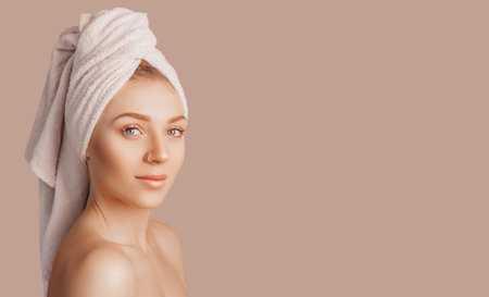 Beautiful sensual young girl with clean skin on a beige background with a mockup. Topless woman in a towel. The concept of spa treatments, natural beauty and care, youth, cream and mask, freshnessの写真素材