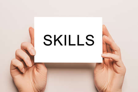 Female hands hold card paper with text SKILLS on a yellow background. Business and finance conceptの写真素材