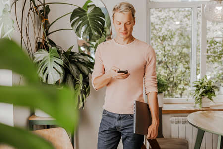 Man checks the phone, businessman with laptop in workspace in eco cafe with plantsの写真素材