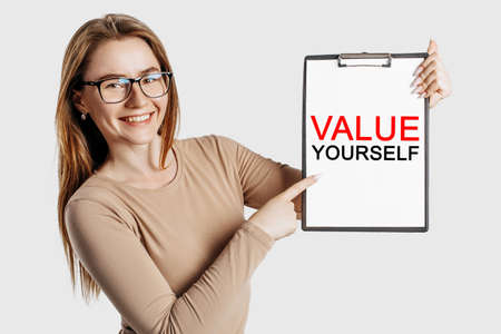 value yourself. Beautiful young business woman wearing glasses holds a clipboard with mock up space isolated on gray backgroundの写真素材