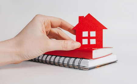 Sweet home. Estimating and paying house tax. Woman holding red house with her hands and notepad in copy space white backgroundの写真素材