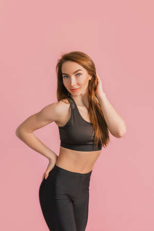 Fitness girl smiling in black sportswear on a pink background. Slim woman with a beautiful athletic body and tanned skinの写真素材