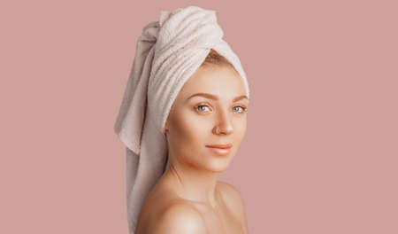 Beautiful sensual young girl with clean skin on a pink background with a mockup. Topless woman in a towel. The concept of spa treatments, natural beauty and care, youth, cream and mask, freshnessの写真素材