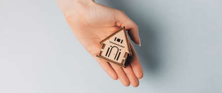 Woman holding a wooden house with her hands with the sun on a light blue background. Sweet homeの写真素材