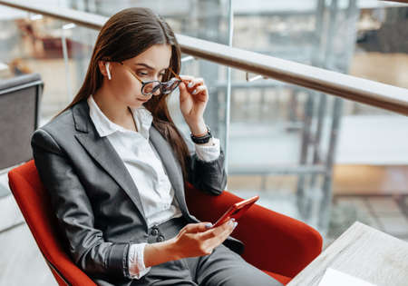 Business woman in glasses at the workplace uses the phone and sits at the table. Manager in the office.の写真素材