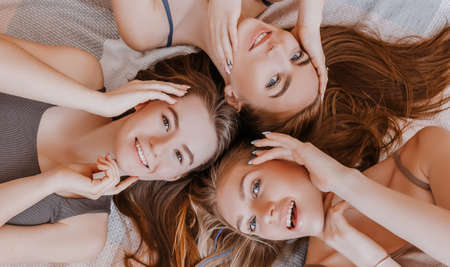 Women rest and have fun. Girlfriends laugh at home lying on the floor on pillows. Tree girls make homemade face and hair beauty masks. Women take care of youthful skin.の写真素材