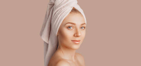 Beautiful sensual young girl with clean skin on a beige background with a mockup. Topless woman in a towel. The concept of spa treatments, natural beauty and care, youth, cream and mask, freshnessの写真素材