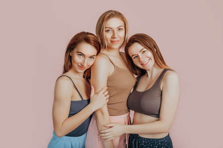 Three girls in comfortable home clothes together on a pink background. Women smile and have fun. The concept of spa treatments, natural beauty and care, youth, cream and mask, freshness, friendshipの写真素材
