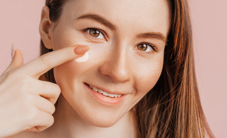 Girl make face beauty masks. Anti-wrinkle cream for the freshness of the skin around the eyes. Woman take care of youthful skin. Model laughing and having fun in spa on pink backgroundの写真素材