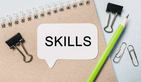 Text SKILLS on a white sticker with office stationery background. Flat lay on business, finance and development conceptの写真素材