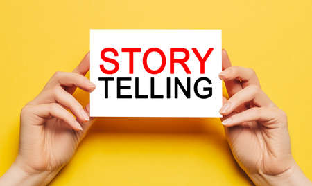 Female hands hold card paper with text Storytelling is the best marketingon a yellow background. Business and finance conceptの写真素材