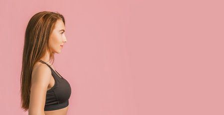 Fitness girl smiling in black sportswear on a pink background. Slim woman with a beautiful athletic body and tanned skinの写真素材