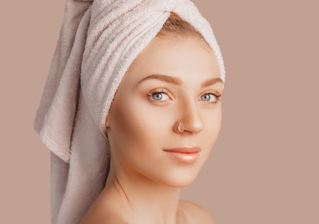 Beautiful sensual young girl with clean skin on a beige background with a mockup. Topless woman in a towel. The concept of spa treatments, natural beauty and care, youth, cream and mask, freshnessの写真素材