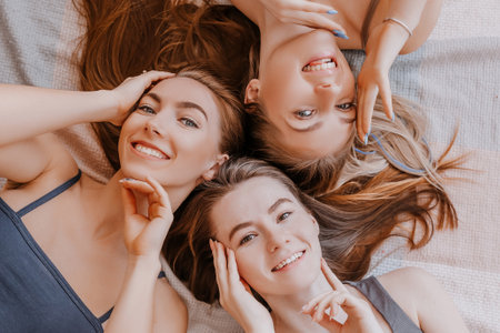 Women rest and have fun. Girlfriends laugh at home lying on the floor on pillows. Tree girls make homemade face and hair beauty masks. Women take care of youthful skin.の写真素材