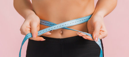 Fitness girl and measures the waist in black sportswear on a pink background. Slim woman with a beautiful athletic body and tanned skinの写真素材
