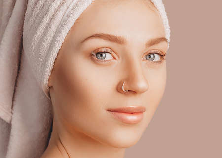 Beautiful sensual young girl with clean skin on a beige background with a mockup. Topless woman in a towel. The concept of spa treatments, natural beauty and care, youth, cream and mask, freshnessの写真素材