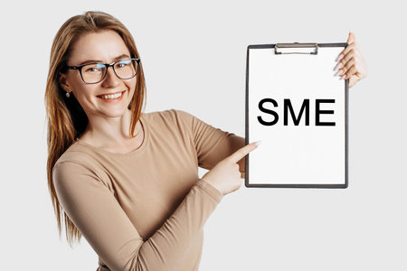 sme. Beautiful young business woman wearing glasses holds a clipboard with mock up space isolated on gray backgroundの写真素材