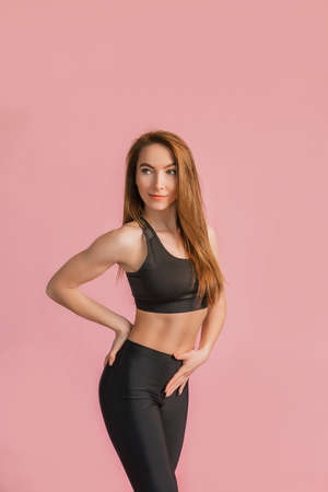Fitness girl smiling in black sportswear on a pink background. Slim woman with a beautiful athletic body and tanned skinの写真素材
