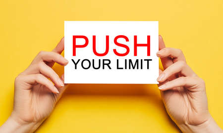 Female hands hold card paper with text PUSH YOUR LIMIT on a yellow background. Business and finance conceptの写真素材