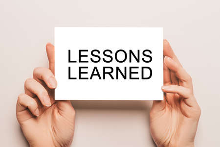 Female hands hold card paper with text LESSONS LEARNED on a yellow background. Education and study conceptの写真素材