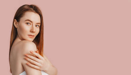 Beautiful sensual young girl with clean skin on a pink background with a mockup. Topless woman in a towel. The concept of spa treatments, natural beauty and care, youth, cream and mask, freshnessの写真素材