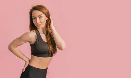 Fitness girl smiling in black sportswear on a pink background. Slim woman with a beautiful athletic body and tanned skinの写真素材