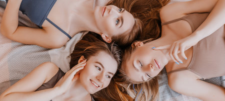 Women rest and have fun. Girlfriends laugh at home lying on the floor on pillows. Tree girls make homemade face and hair beauty masks. Women take care of youthful skin.の写真素材