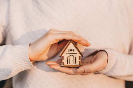 Woman holding a wooden house with her hands with the sun on a light pink background. Sweet homeの写真素材