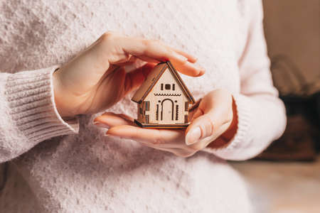 Woman holding a wooden house with her hands with the sun on a light pink background. Sweet homeの写真素材