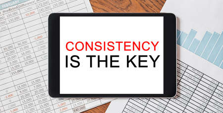 Tablet with text Consistency is the key on your desktop with documents, reports and graphs. Business and finance conceptの写真素材