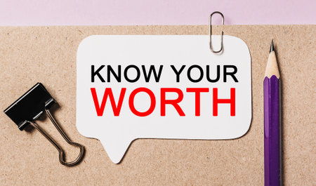 Text KNOW YOUR WORTH on a white sticker with office stationery background. Flat lay on business, finance and development conceptの写真素材