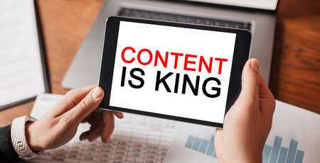 Man hands holding tablet with text Content is King at workplace. Businessman working at desk with documentsの写真素材
